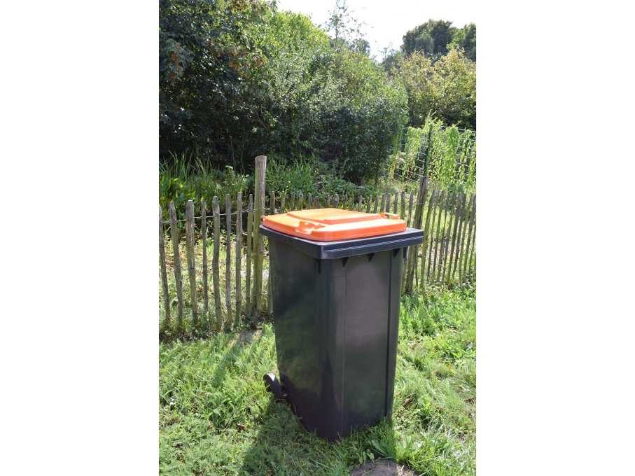 Das Bild zeigt eine Wertstofftonne. Eine schwarze Tonne mit orangem Deckel